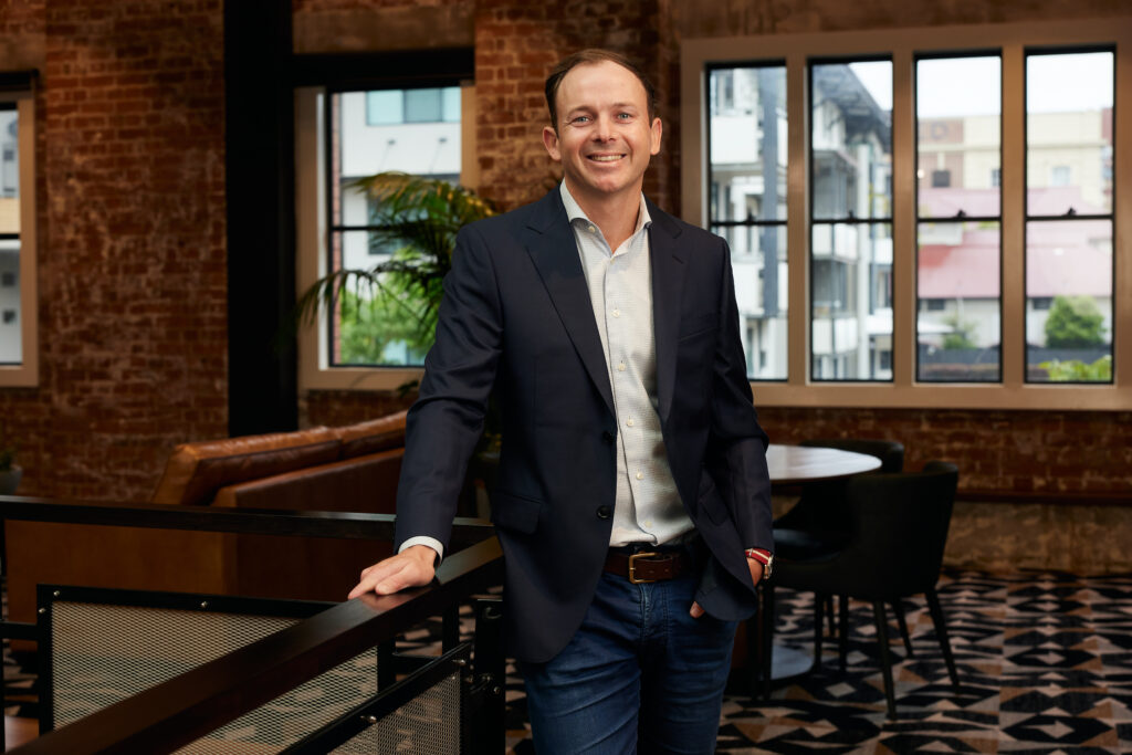 A man in a suit stands in a classy brick room