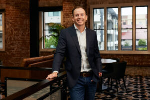 A man in a suit stands in a classy brick room